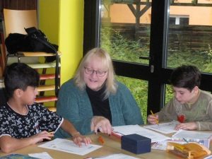 Ehrenamtliche Mitarbeiterin des MGH bei der Hausaufgabenhilfe mit Flüchtlingskindern der Übergangsklasse in der Mittelschule Röthenbach. Foto: Caritas