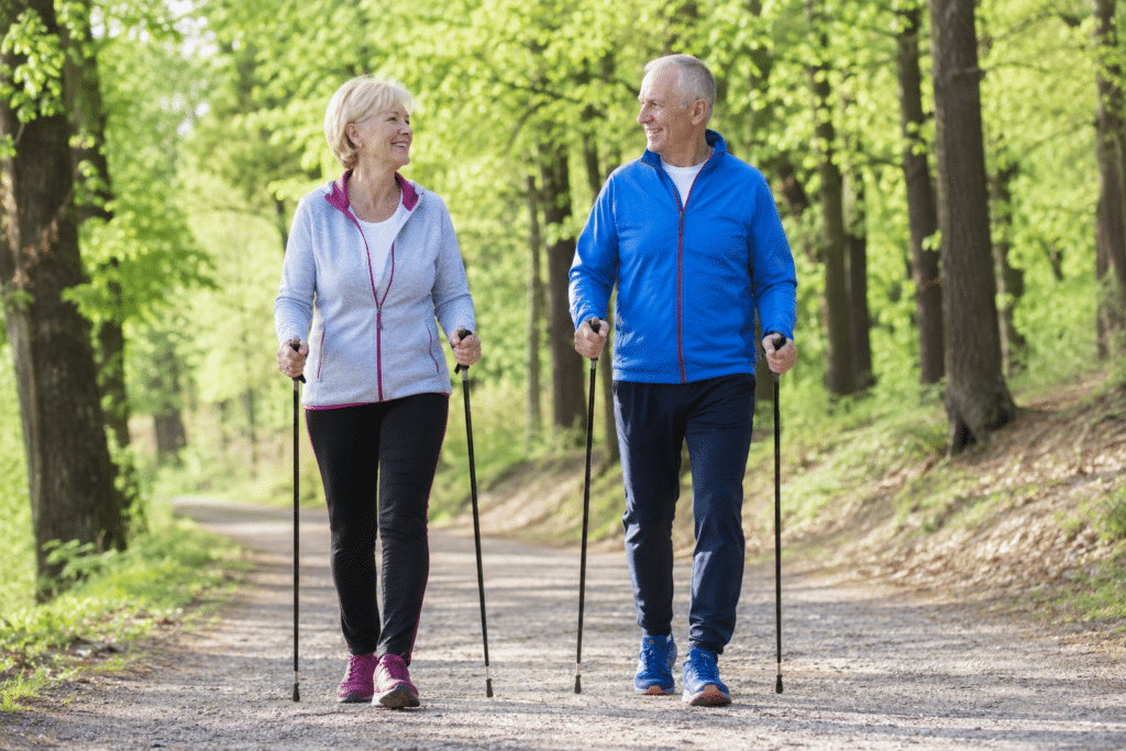 Eine ältere Frau und ein älterer Mann spazieren mit Nordic Walking Stöcken im Wald.